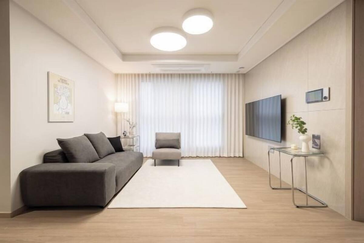 A modern living room with a sofa, armchair, TV, and a small table.