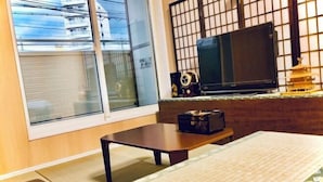 A room with a sliding glass door, a television on a stand, a small table, and a bed with a patterned bedspread. - Kannosu NO.1 (Osaka)