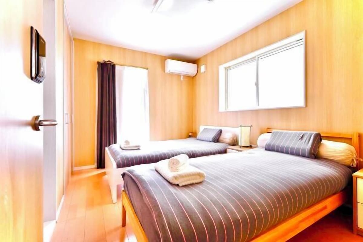 A hotel room with two beds, a window, an air conditioning unit, and a door.