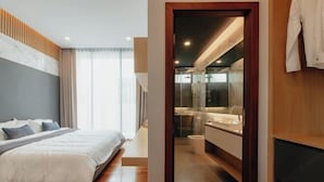 A bedroom with a bed, a bedside table, and a view of a bathroom with a mirror and sink.