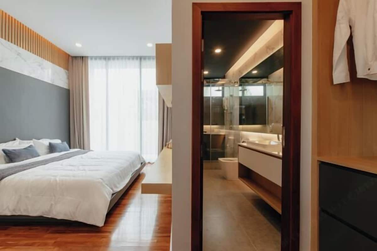 Ein Schlafzimmer mit Bett, Nachttisch und Blick auf ein Badezimmer inklusive Spiegel und Waschbecken.