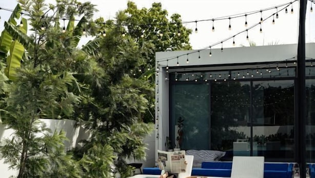 A modern outdoor pool area with a glass enclosure, string lights, and a seating area with cushions.