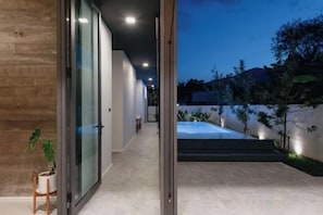 Un interior modern amb una porta de vidre que dona a zona exterior, una planta en test i una escala.