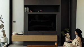 A modern living room with a large flat-screen TV, a wooden coffee table, and a person reading a book.
