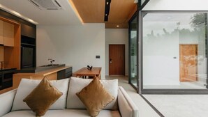 A modern living room with a sofa, a coffee table, and a glass wall offering a view of the outdoors.