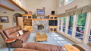 A cozy living room with a fireplace, leather sofas, a coffee table, and a stone wall. - River Bend Retreat (Bonneville County)