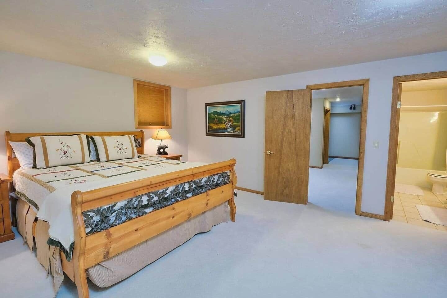 Una camera da letto con un letto in legno, un comodino con una lampada, un quadro appeso al muro e una porta che dà su un'altra stanza.