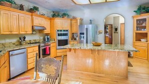 A kitchen with wooden cabinets, a central island, stainless steel appliances, and a dining area with a chair. - River Bend Retreat (Bonneville County)