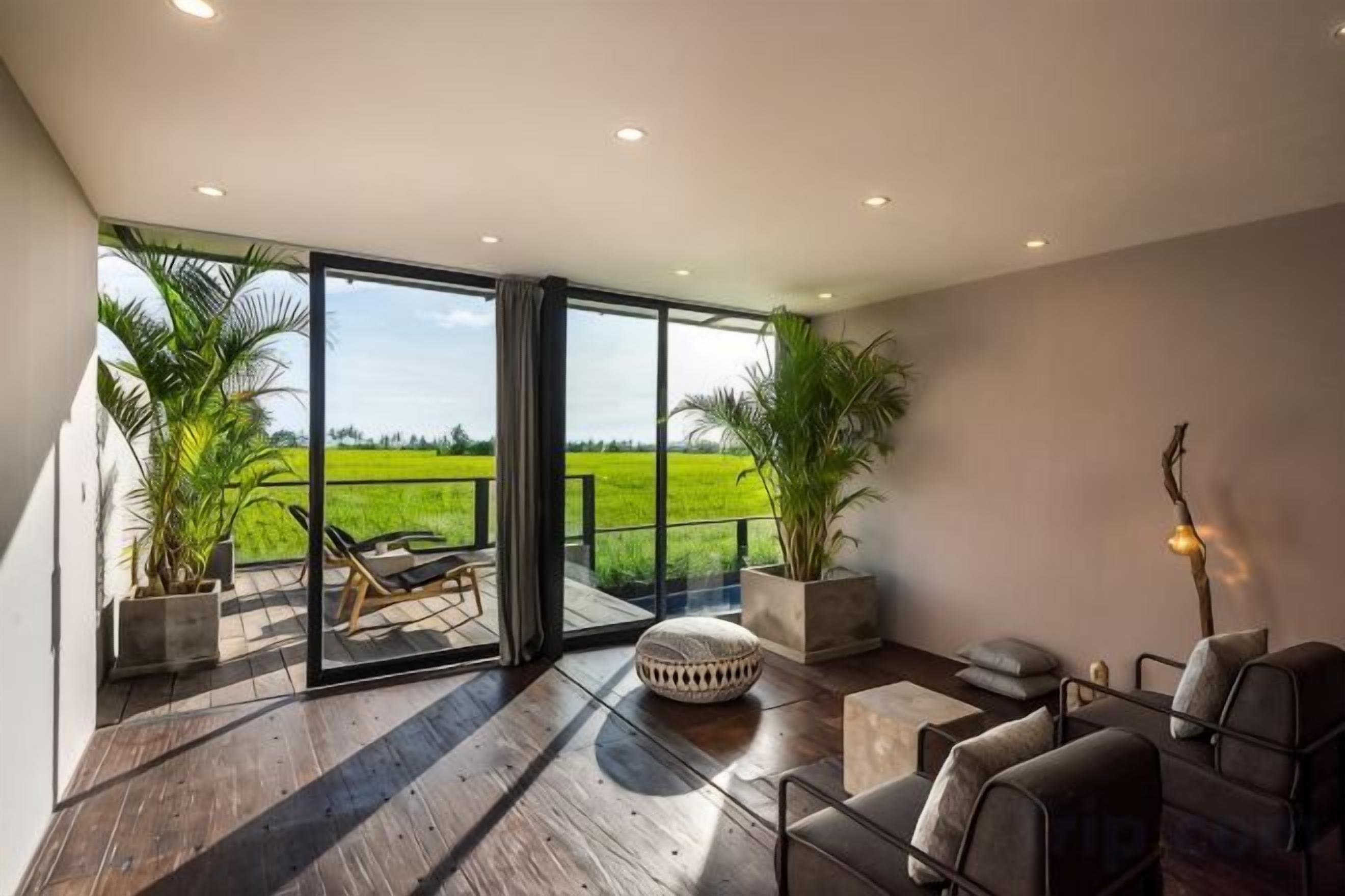 A spacious room with a large sliding glass door leading to a balcony, wooden flooring, and a seating area with a sofa and chairs.