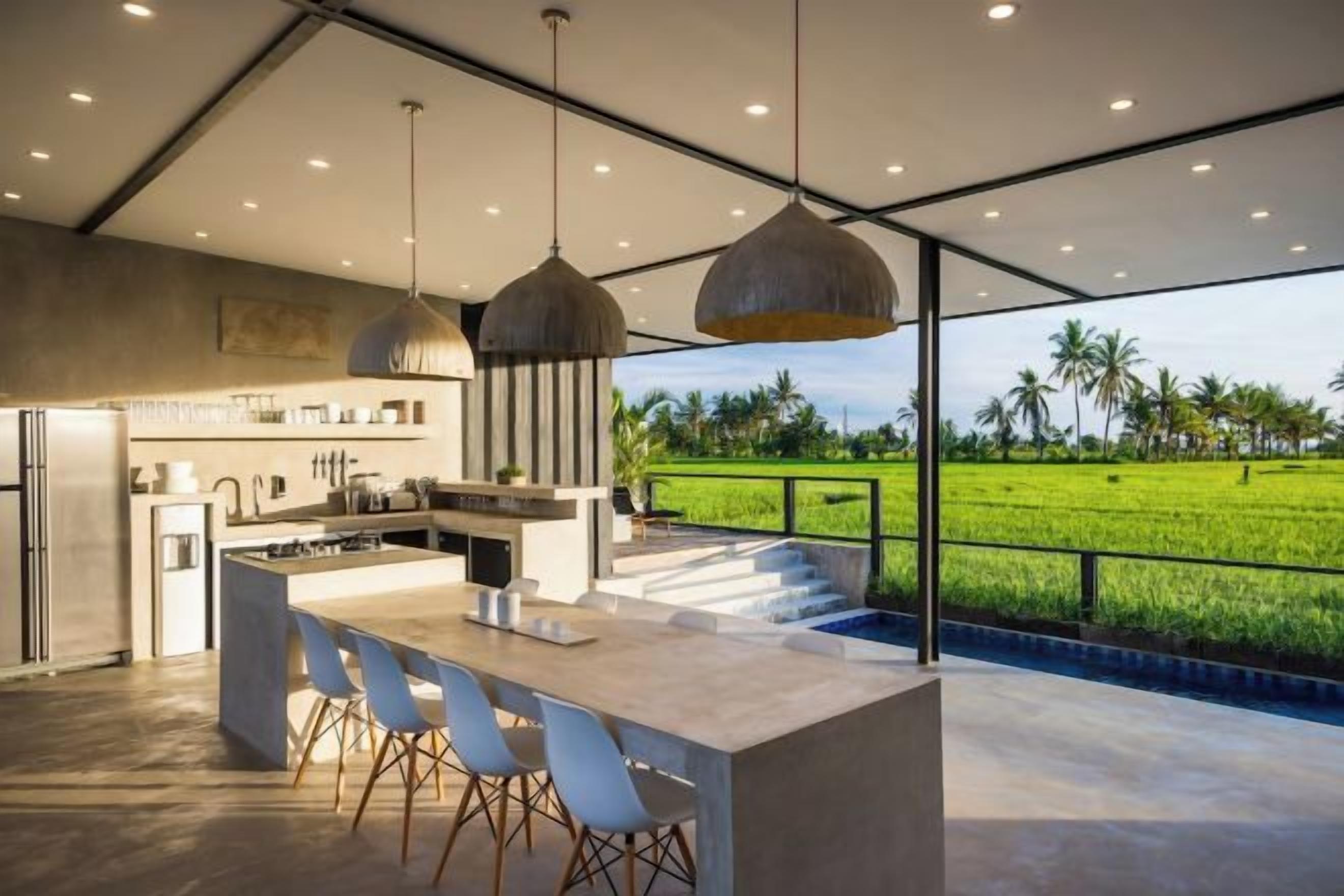 A modern kitchen with a large island, pendant lighting, and a view of a green field.