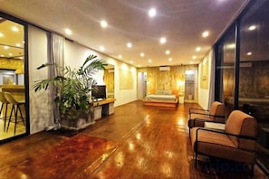 A spacious room with a wooden floor, a bed, a seating area with chairs, and a large window.