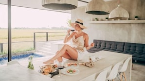 A dining area with a pool view, a sofa, and hanging pendant lights. - Samsara Villa with Rice Field View (Bali)