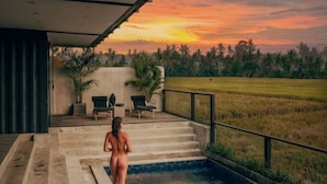 A person standing by a pool with a sunset view. - Samsara Villa with Rice Field View (Bali)