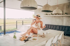 A person dining at a table with a view of a pool and fields, in a modern interior with pendant lighting. - Samsara Villa with Rice Field View (Bali)