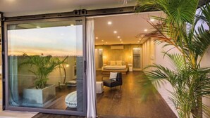 A modern living room with a sofa and a coffee table, a sliding glass door leading to a balcony with plants, and a view of the sunset. - Samsara Villa with Rice Field View (Bali)
