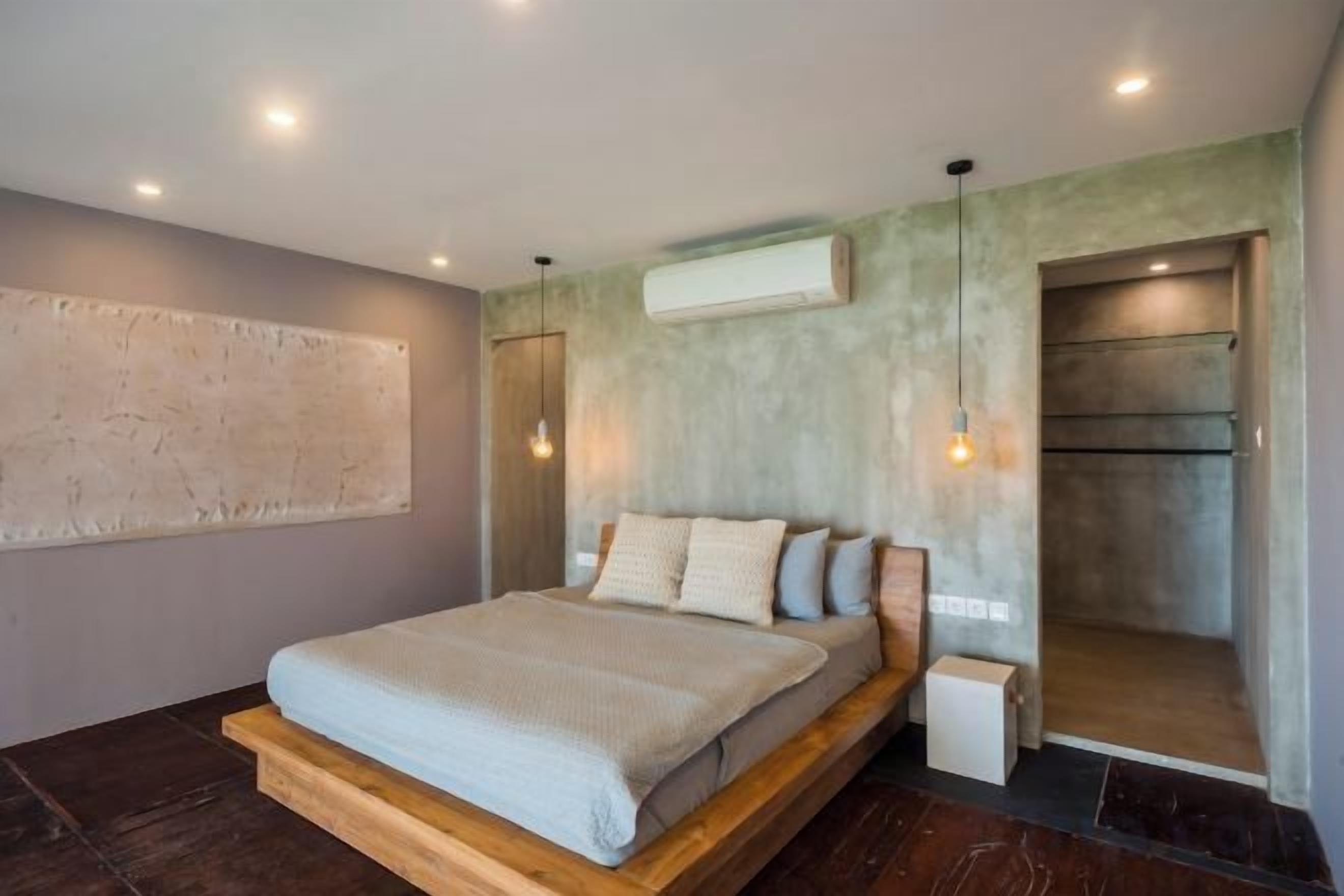 A modern bedroom with a large bed, a built-in bench, a wall-mounted air conditioner, and a hanging light fixture.