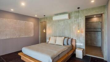 A modern bedroom with a large bed, a built-in bench, a wall-mounted air conditioner, and a hanging light fixture.
