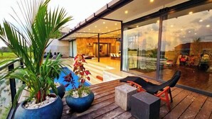 A modern outdoor area with a wooden deck, seating, and potted plants. - Samsara Villa with Rice Field View (Bali)