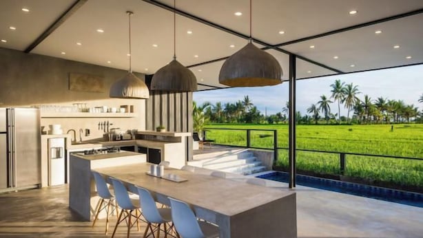 A modern kitchen with a large island, bar stools, pendant lighting, and a view of a green field. - Samsara Villa with Rice Field View (Bali)