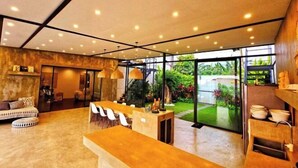 A modern interior with a kitchen area, dining space, and a view of a garden. - Samsara Villa with Rice Field View (Bali)