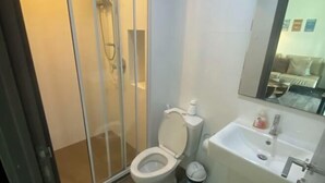 A modern bathroom with a glass shower enclosure, a toilet, and a sink with a mirror above. - BRAND New Sukhumvit Condo Cozy BTS (Bangkok)