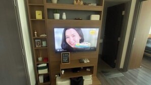 A television on a wooden stand with shelves above it, a small plant, and a door to the right. - BRAND New Sukhumvit Condo Cozy BTS (Bangkok)