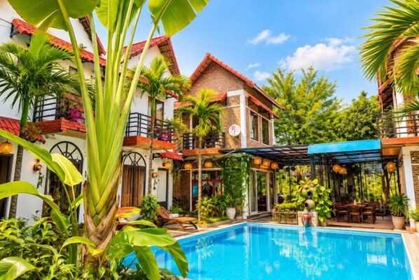 A two-story building with a swimming pool, surrounded by lush greenery and a clear blue sky. - Tam Coc Mandala Homestay & Pool (Hoa Lu District)
