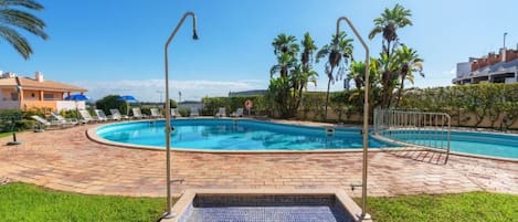 A swimming pool with a hot tub, surrounded by palm trees and a brick patio.