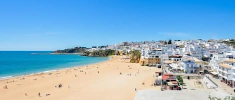 A coastal town with a sandy beach, buildings along the shore, and a clear blue sky.