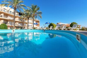 A swimming pool with lounge chairs and umbrellas, surrounded by palm trees and a building with balconies. - BnB Homes Apartment with cozy Terrace & Swimming pool near the heart city (Albufeira)