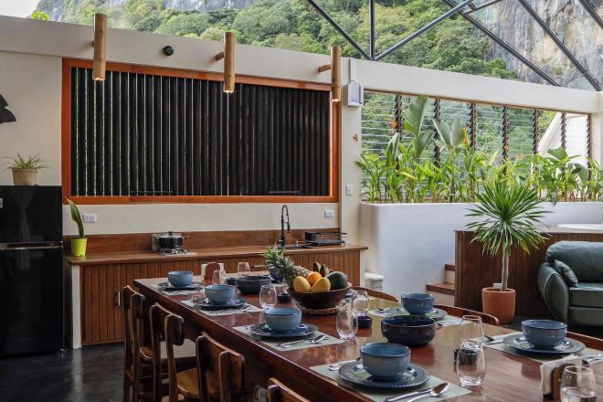 A modern kitchen with a wooden table set for dining, a black refrigerator, and a large window overlooking a lush garden.