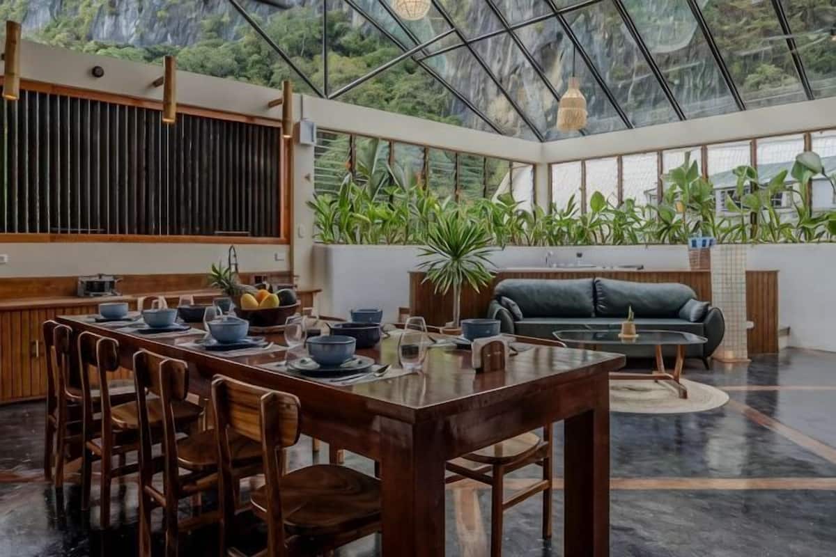 A spacious room with a dining area, a sofa, and a large window with a view of greenery.