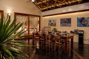 A dining area with a wooden table and chairs, a large plant, and artwork on the walls. - Unique space: The Glass House (El Nido)