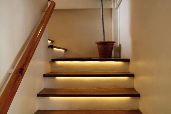 A staircase with wooden steps and a wooden handrail, illuminated by under-cabinet lighting. - Unique space: The Glass House (El Nido)