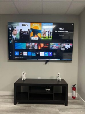 A flat-screen TV mounted on a wall above a black entertainment unit with two small white figurines on top.
