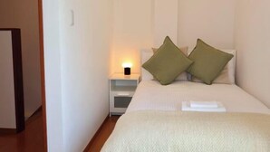A bedroom with a bed, pillows, a nightstand with a lamp, and a white wall. - Orange House Tsuruhashi｜With Garage, Accommodates 8 People (Osaka)