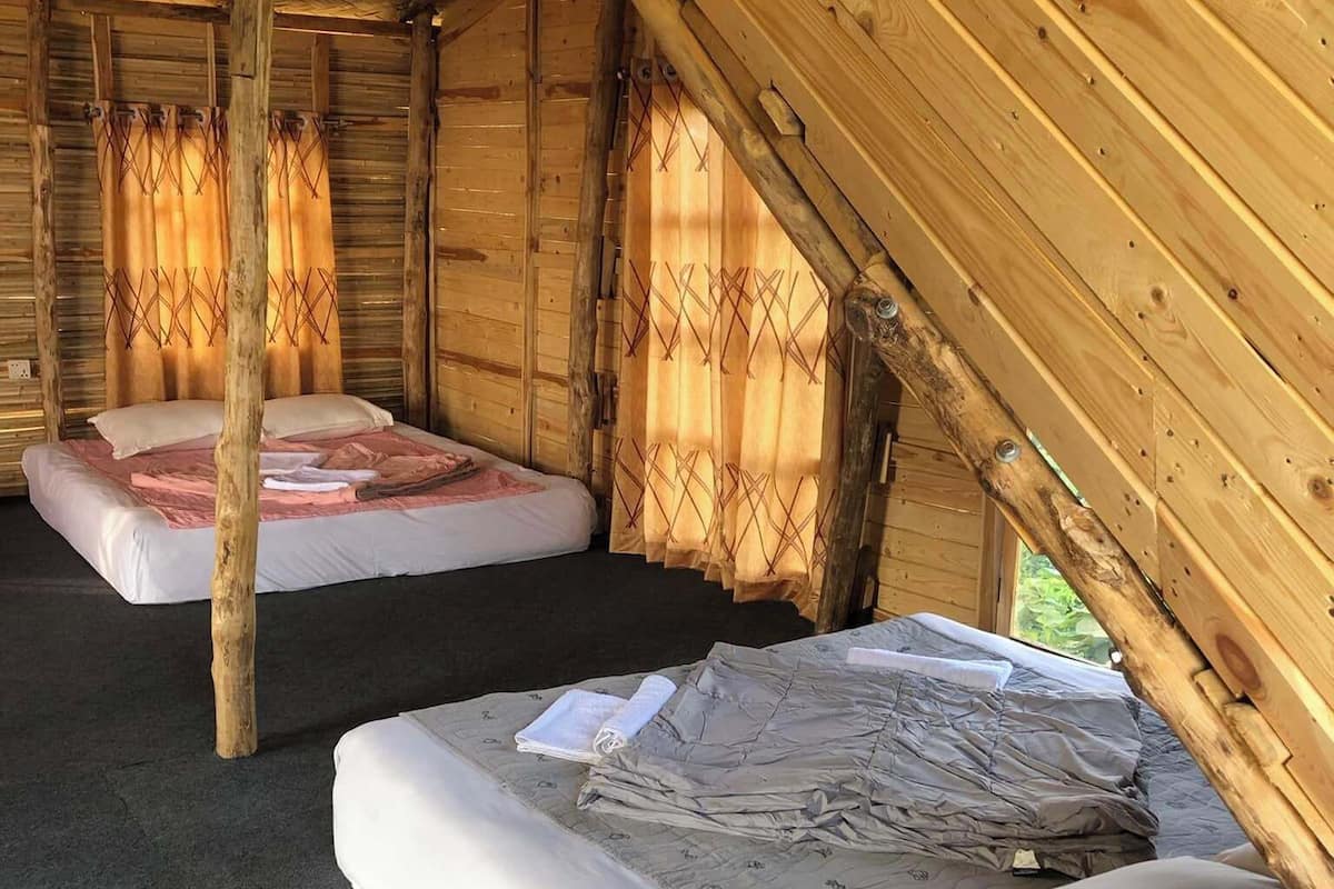 A rustic wooden cabin with two single beds, each with a mattress and pillows.