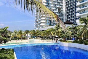 A swimming pool with a view of a high-rise hotel and palm trees. - 2 BR Penthouse w/ Wide Balcony and 7ft Billiards (San Fernando)
