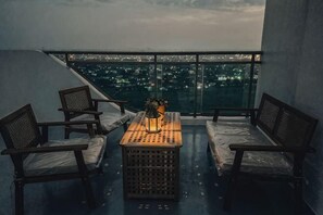 Een balkon met een tafel, stoelen en uitzicht op een stadsbeeld in de nacht.