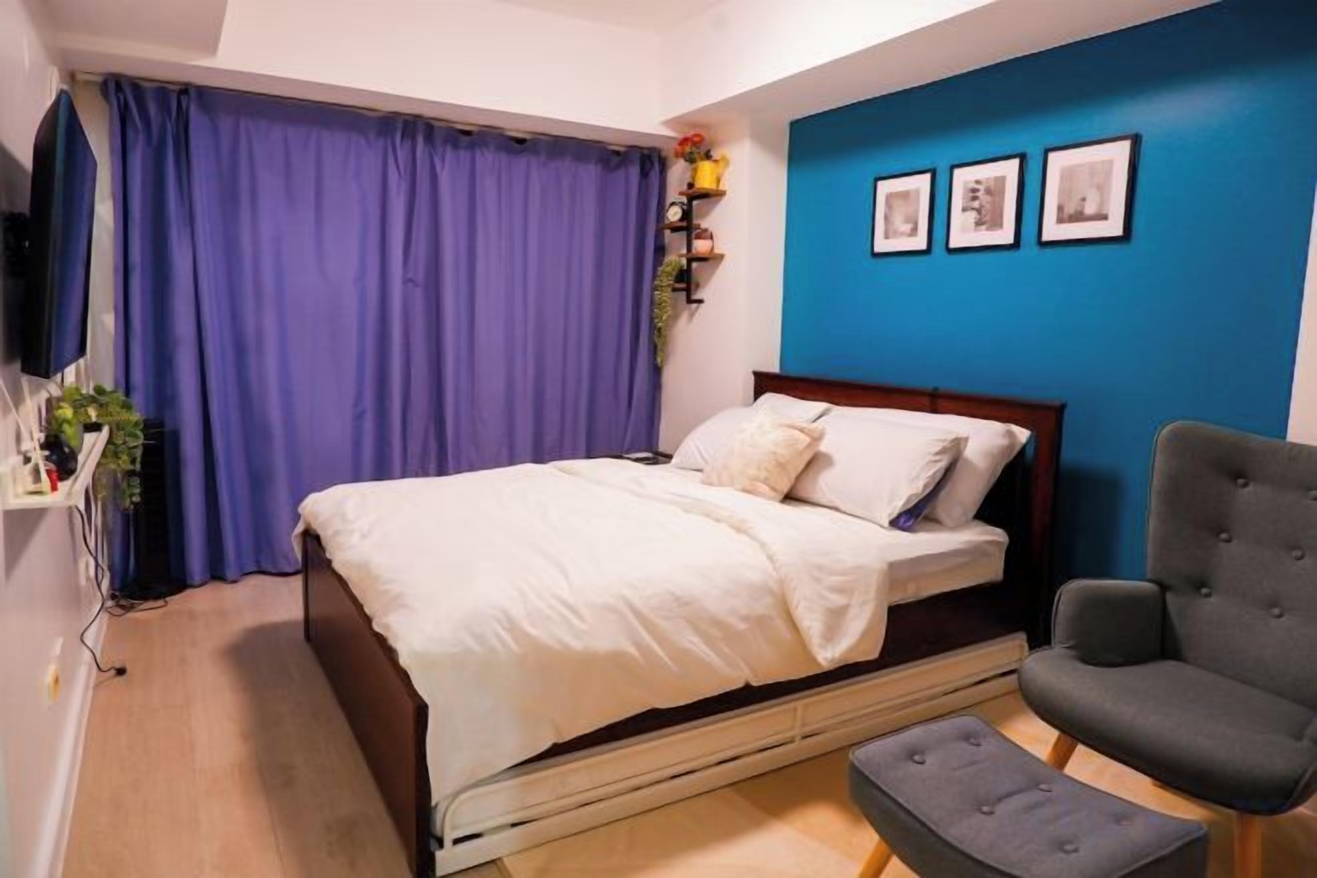 A bedroom with a bed, a chair, a TV, and a blue wall with pictures.