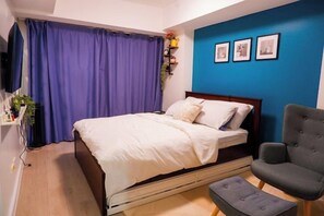 A bedroom with a bed, a chair, a TV, and a blue wall with pictures. - 2 BR Penthouse w/ Wide Balcony and 7ft Billiards (San Fernando)