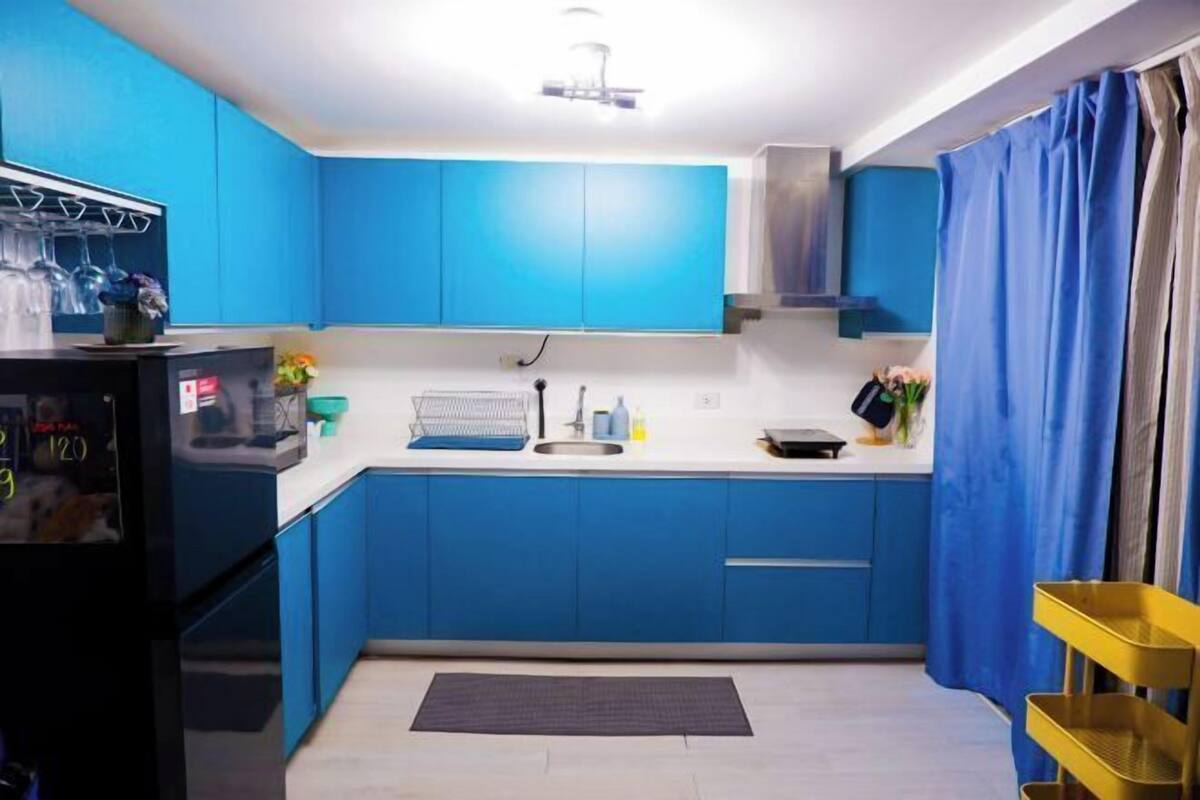 A kitchen with blue cabinets, a black refrigerator, a sink, and a yellow shelf.