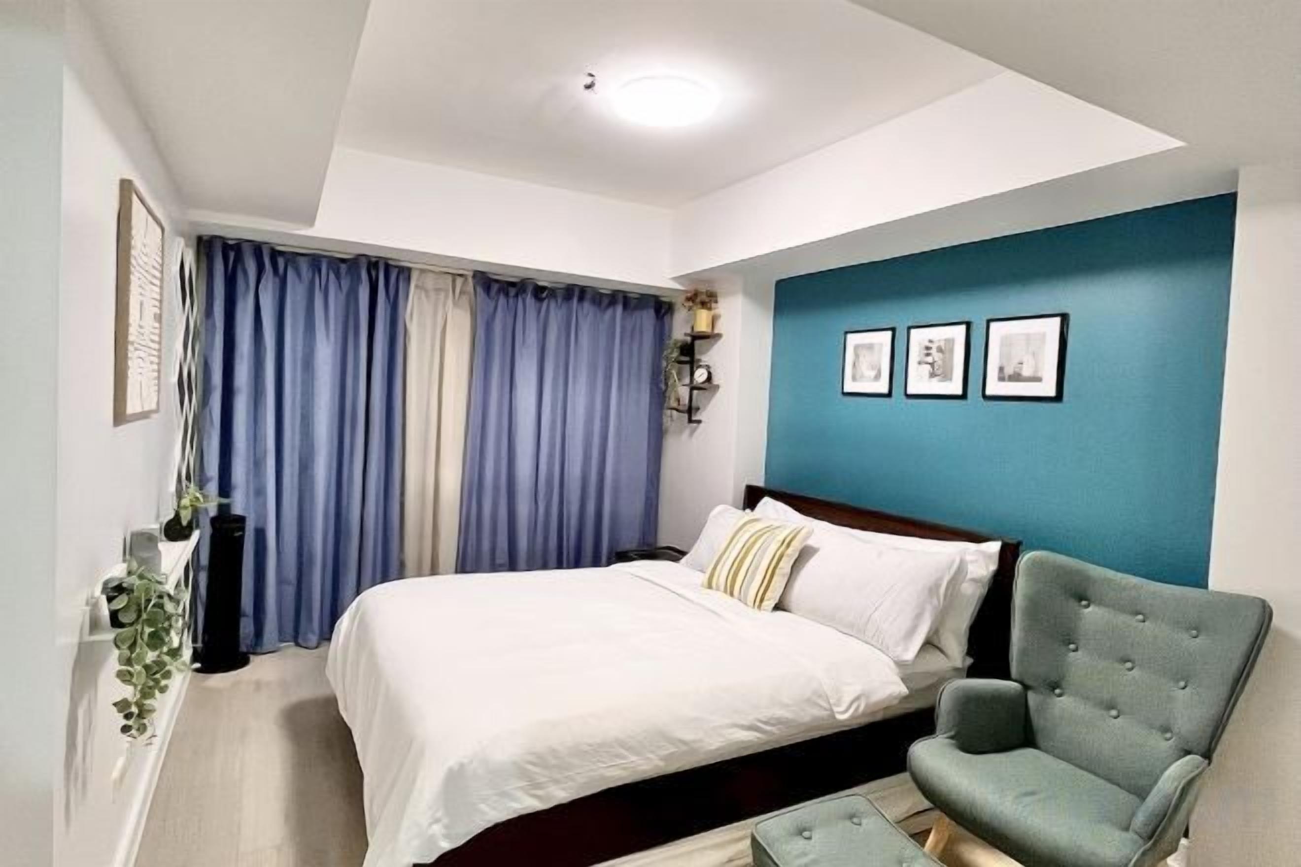 A bedroom with a bed, a chair, a window with curtains, and wall-mounted pictures.