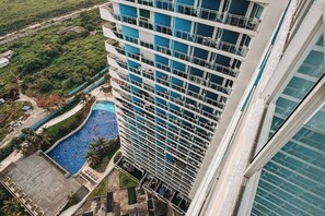 A high-rise building with multiple balconies, a swimming pool, and a view of the surrounding greenery. - 2 BR Penthouse w/ Wide Balcony and 7ft Billiards (San Fernando)