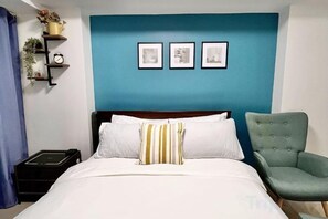 A bed with white bedding and a striped pillow, a green armchair, and a wall with three framed pictures. - 2 BR Penthouse w/ Wide Balcony and 7ft Billiards (San Fernando)