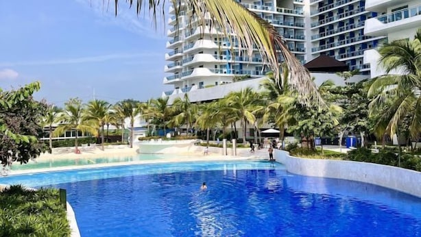 A swimming pool surrounded by palm trees and a high-rise hotel building. - 2 BR Penthouse w/ Wide Balcony and 7ft Billiards (San Fernando)