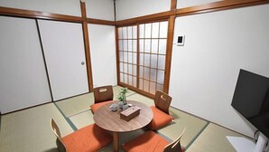 A traditional Japanese room with tatami flooring, a low table with cushions, a sliding door, and a television. - Bunka 1 chome (Tokyo)