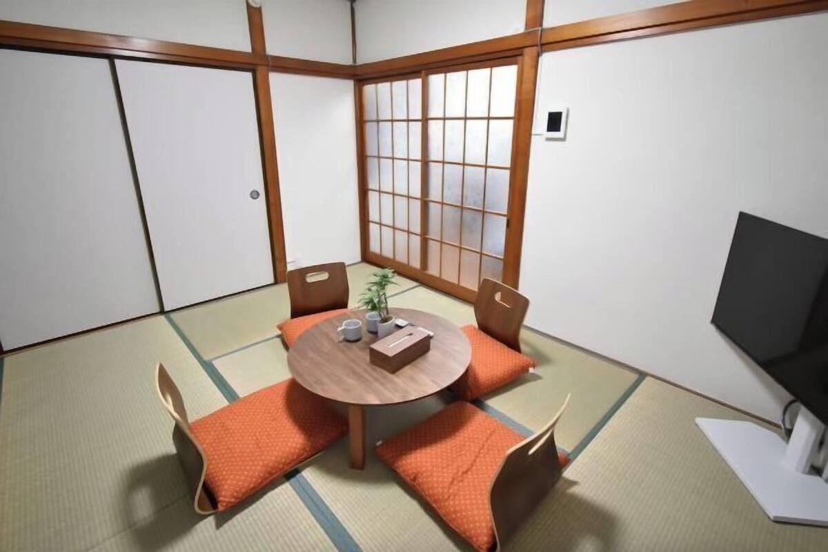 A traditional Japanese room with tatami flooring, a low table with cushions, a sliding door, and a television.