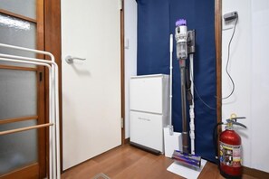 Ένα δωμάτιο με ένα λευκό καλοριφέρ, μια μπλε κουρτίνα, μια λευκή πόρτα και έναν πυροσβεστήρα.