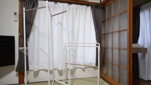 A corner room with a white metal drying rack, a sliding glass door with curtains, and a wooden floor. - Bunka 1 chome (Tokyo)